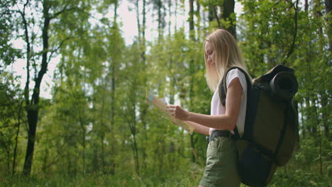 Young-woman-traveler-with-map-and-backpack-relaxing-outdoor-at-Nature-trail-on-summer-vacations-day.-Lifestyle-hiking-concept.-Wood-trip.-Picking-direction-with-a-map.